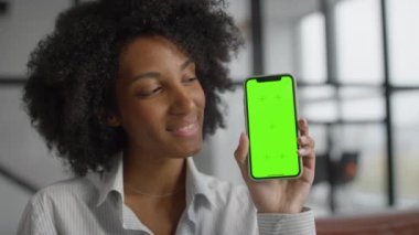 Neşeli bir kadın elinde yeşil ekran gösteren bir akıllı telefon tutuyor, modern bir ofiste kişiselleştirilebilir içerik için yer tutucu sunuyor..