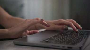 Çevrimiçi dizüstü bilgisayarda yazı yazan ve tarayan yeşil tırnaklı bir kadının elleri modern ve odaklanmış bir sahne yaratıyor..