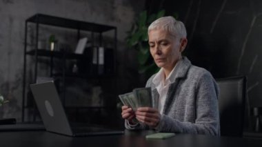 Bilgisayarında notlar alırken dolar sayan, modern ve loş bir ofiste çalışan son sınıf öğrencisi bir kadın..