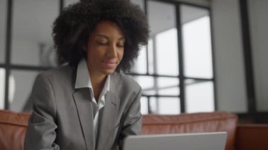 Gri takım elbiseli profesyonel bir kadın laptopuyla modern bir ofis alanında özenle çalışıyor..