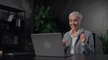 Modern ofis ortamında laptopunda başarıyı kutlarken heyecan ve neşe ifade eden olgun bir iş kadını..