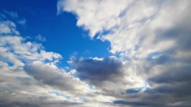 Kabarık beyaz ve koyu renkli bulutların dinamik zaman çizelgesi canlı mavi bir gökyüzünde hareket ediyor..