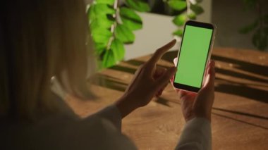 Kadın eli yeşil ekran akıllı telefonuna el hareketi yapıyor. Arka planda doğal ışık ve yeşil bitkiler var..