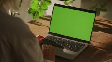 Bir kadın, içi boş yeşil ekranlı bir dizüstü bilgisayar kullanıyor. Güneş ışığı ve bitkiler doğal bir zemin oluşturur..