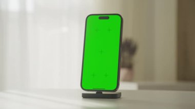 Yeşil ekran yer tutuculu modern bir akıllı telefon beyaz bir yüzey üzerindeki şarj limanında oturmakta, kişiselleştirmeye veya modellemeye hazır..