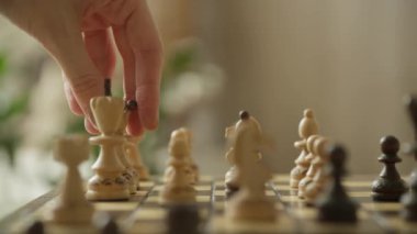 Bir el yakın plan satranç tahtasında tahta bir satranç kraliçesini hareket ettiriyor. Oyun oyununda strateji, zeka ve karar verme mekanizmasını sembolize ediyor..