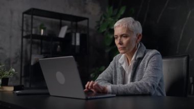 Profesyonel bir ofisteki kıdemli bir iş kadını interneti bilgisayarında geziyor. Odaklanmış ve internetten araştırma yapıyormuş gibi görünüyor..