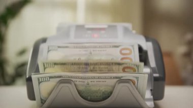 100 dolarlık banknotları sayan, finans, bankacılık, nakit yönetimi ve mali işlemleri sembolize eden bir para sayma makinesinin yakın çekimi.