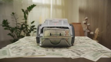 100 dolarlık banknotlarla dolu bir para sayma makinesi, etrafa saçılmış paralar, zenginlik, bankacılık ve finansal işlemleri sembolize ediyor..