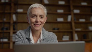 Dizüstü bilgisayarına bakan, modern bir ofiste online bir toplantı ya da video konferansına katılan, kısa beyaz saçlı, mutlu kıdemli iş kadını..