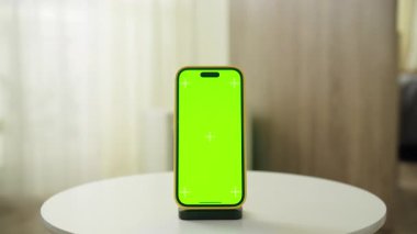 Bir tribüne yerleştirilmiş yeşil ekran akıllı telefon, sinematik bir hareketle görüntüleniyor, modeller, dijital içerik ve görsel efektler için ideal.
