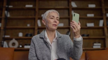 Son sınıf öğrencisi bir kadın akıllı telefonunu tutarken, video ya da teknik bir sorunla boğuşurken hayal kırıklığına uğramış gibi görünür..