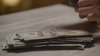 Masadaki bir yığın Amerikan doları banknotunu sayarken çekilmiş detaylı bir yakın çekim. Maliye, zenginlik ve para yönetimini simgeliyor..
