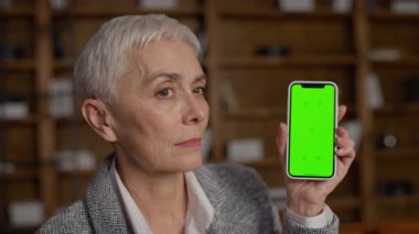 Üst düzey bir kadın yeşil ekranlı akıllı telefonu elinde tutarken onaylıyor, modeller, uygulama promosyonları veya dijital içerik için ideal.