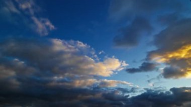 Gün batımında gökyüzünde kayan bulutların zaman çizelgesi, altın ve mavi renkler dinamik ve dramatik bir atmosfer yaratıyor..