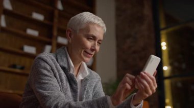 Samimi bir ofis ortamında akıllı telefonunu kullanırken gülümseyen, iletişim kuran ya da mesajları kontrol eden üst düzey profesyonel bir kadın..