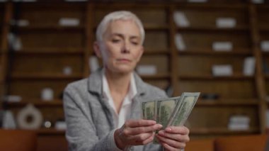 Modern bir ofiste oturan, finans, servet ve bütçeyi temsil eden bir yığın Amerikan dolarını dikkatle sayan üst düzey profesyonel bir kadın..