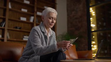 Ofiste para sayan kıdemli iş kadını, modern bir ofiste oturan, bilgisayarında çalışırken nakit sayan, finansal yönetimi, iş gelirlerini sembolize eden olgun profesyonel bir kadın.