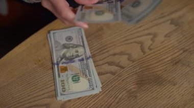 Yakın plan çekimler, tahtadan bir masanın üzerinde servet, finans ve nakit işlemlerini temsil eden 100 dolarlık banknotları saymak ve organize etmek..