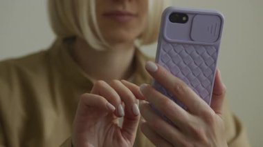 Elinde mor bir çantayla akıllı bir telefon tutan bir kadın. Kapalı bir ortamda otururken ekranla etkileşime geçiyor..