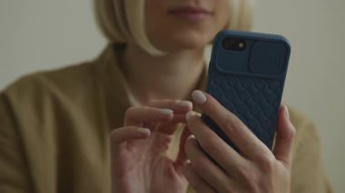 Akıllı telefonu dokulu mavi koruyucu bir çantayla elinde tutan bir kadın, kapalı bir ortamda ekranla etkileşime geçiyor..