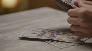 Masadaki yüz dolarlık banknotları karıştıran, zenginliği, finans ve nakit işlemlerini temsil eden yakın plan bir el..