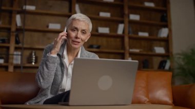 Olgun bir iş kadını laptopuyla çalışırken bir telefon görüşmesi yapmış ve ev ofisinden güvenli bir şekilde hizmet satmış..