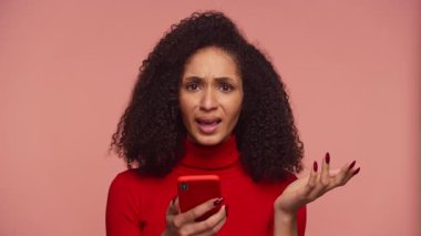 Kırmızı kazaklı bir kadın, internet alışverişi ya da ödemeyle ilgili bir soruna tepki olarak akıllı telefonunu sinirli ve hayal kırıklığına uğramış bir ifadeyle tutuyor..