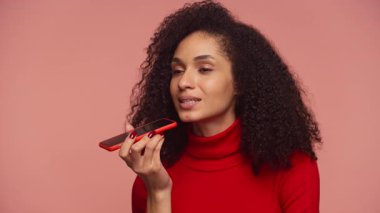 Kırmızı balıkçı yakalı bir kadın akıllı telefonuyla konuşur, bir sesli mesaj kaydeder ya da pembe arka planda ses asistanı kullanır..