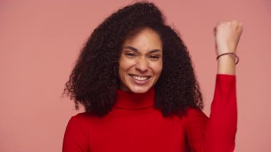 Kırmızı balıkçı yakalı neşeli bir kadın ışıl ışıl gülümser ve kutlama için yumruğunu kaldırır, heyecanını, zaferini veya başarısını ifade eder..