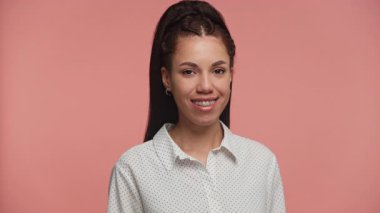 Dişlerinde diş teli olan gülümseyen genç bir kadının portresi, pembe arka planda beyaz bir benekli gömlek giyiyor..