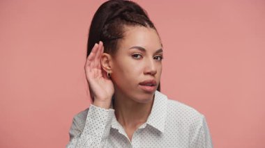 Elini kulağına odaklanmış bir ifadeyle tutan genç bir kadın, pembe bir arka plana karşı dinleme ya da dinlemeyi sembolize ediyor..