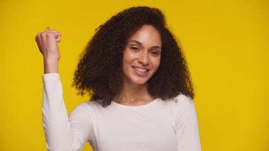 Heyecanlı Afrikalı Amerikalı kadın zafer için gülümseyen ve yumruğunu kaldıran, fotokopi çekilen parlak sarı arka plandaki kameraya bakan.
