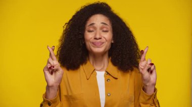 Gözleri kapalı ve parmakları çapraz olan genç bir kadın, umudunu ifade ediyor ya da özenli sarı bir zemin üzerinde hayal kuruyor..