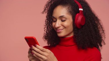 Kulaklık takan, gülümseyen ve akıllı telefondan mesaj yazan neşeli genç bir kadın..