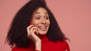 Neşeli bir telefon görüşmesi yapan mutlu genç bir kadın, gülümseyen ve gülen bir yandan da elinde pembe arka planla fotokopi çekilen bir akıllı telefonu tutan..