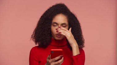 Hayal kırıklığına uğramış genç bir kadın akıllı telefon tutuyor ve yüzünü hayal kırıklığı ya da strese sokuyor..