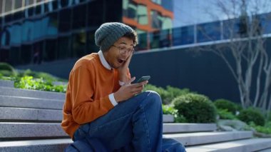 Mutlu öğrenci, akıllı telefondan harika haberler okurken, dışarıda kampüsün yakınındaki basamaklarda otururken şok ve neşeyle tepki veriyor..