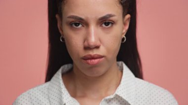 Kızgın Afro-Amerikalı kadının yakın plan portresi. Kameraya yoğun, hoşnutsuz bir ifadeyle bakıyor. Pembe arka planda izole edilmiş..