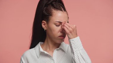 Hüsrana uğramış kadın burnunun köprüsünü sıkıyor, gözleri kapalı, pembe arka planda baş ağrısı ya da migrenden dolayı acı ya da rahatsızlık gösteriyor..