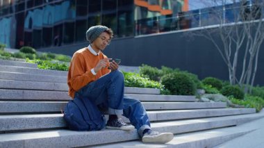 Rahat genç adam şehir basamaklarında sırt çantasıyla oturuyor, akıllı telefonuyla internette geziniyor ya da geziniyor..