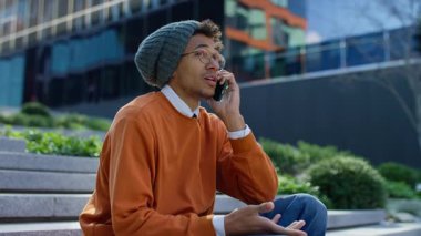 Endişeli genç adam şehir basamaklarında oturuyor, endişeli ya da kafası karışık bir şekilde şehir ortamında telefon görüşmesi yapıyor..