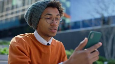 Gözlüklü ve bereli bir delikanlının şehirde dışarıda otururken akıllı telefonuyla yaptığı bir video görüşmesi..