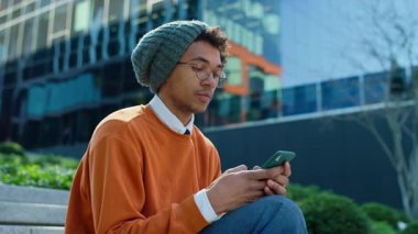 Gündelik kıyafetli genç bir üniversite öğrencisi kampüs binasının yakınındaki telefonuna bir mesaj yazmaya odaklanmış..
