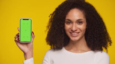 Beyaz bluzlu, kendine güvenen genç bir kadın yeşil ekran ekranlı akıllı bir telefon tutuyor. Uygulama modelleri ya da reklamlar için mükemmel..