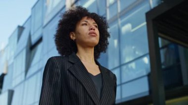 İnce çizgili takım elbiseli kararlı profesyonel bir kadın modern cam bir binanın önünde işe doğru yürüyor, odaklanmış ve güçlenmiş görünüyor..