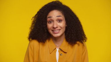 Şaşkın kadın omuzlarını silker ve kaşlarını kaldırır. Parlak sarı bir arka plana karşı kafa karışıklığı ya da belirsizlik gösterir..