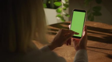 Yeşil ekranlı akıllı telefonu kullanan, ekranın içeriğini dikkatle izlerken tek bir kaydırma hareketi yapan bir kadının yakın çekimi.