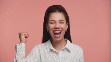 Heyecanlı genç bir kadın gülümseyerek ve kutlamada yumruğunu kaldırarak, kişisel bir hedefe ulaştıktan sonra sevinç ve gurur ifade ediyor..