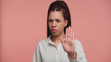 Sert bir ifadeyle elini kaldıran genç bir kadın, pembe arka plana karşı onaylamadığını ya da reddettiğini işaret ediyor..